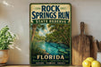 A vintage-style sign for the Rock Springs Run State Reserve in Florida, featuring a scenic illustration of a river surrounded by palm trees and lush greenery.