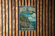 A vintage-style sign for Rocky Arbor State Park in Wisconsin, featuring a scenic landscape with pine trees, a rocky cliff, and a body of water.