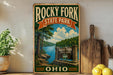 A vintage-style sign for Rocky Fork State Park in Ohio, featuring a scenic landscape with a river, trees, and a wooden signpost.