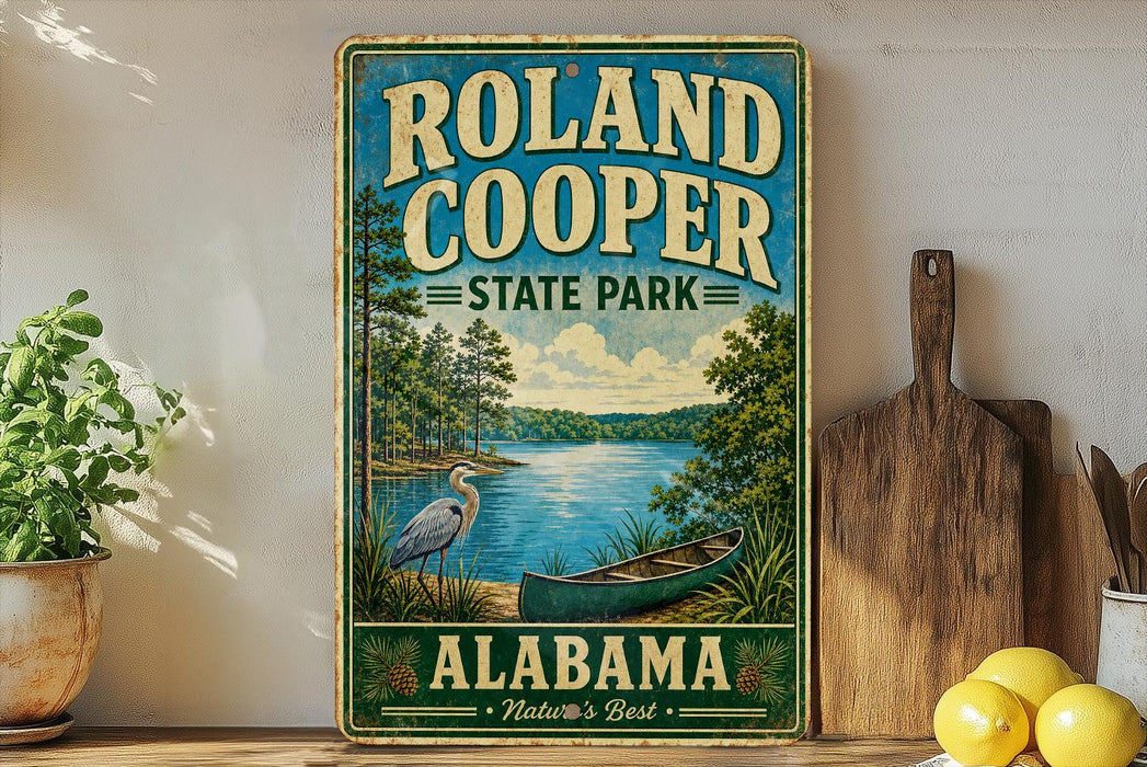 A vintage-style sign for Roland Cooper State Park in Alabama, featuring a scenic illustration of a lake, a crane, and a canoe.