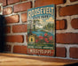 A vintage-style metal sign for Roosevelt State Park, featuring a scenic landscape with a lake, trees, and flowers, mounted on a brick wall.
