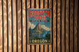 A vintage metal sign for Rooster Rock State Park in Oregon, featuring a mountain landscape and the text "Rooster Rock State Park Oregon".