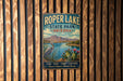 A vintage metal sign for Roper Lake State Park, Arizona, featuring a scenic landscape with mountains, a lake, and various flora.