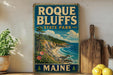 A vintage-style metal sign for Roque Bluffs State Park in Maine, featuring a scenic coastal landscape with pine trees, cliffs, and a beach.