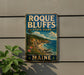 A vintage-style metal sign for Roque Bluffs State Park in Maine, featuring a scenic coastal landscape with a rocky cliff, pine trees, and a body of water.