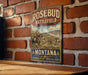 A vintage-style metal sign with the text "ROSEBUD BATTLEFIELD STAY PARK MONTANA" is displayed on a brick wall.