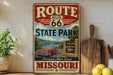A vintage-style metal sign for Route 66 State Park in Missouri, featuring a red convertible car and scenic landscape.