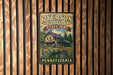 A vintage-style metal sign for Ryserson Station State Park in Pennsylvania, featuring a scenic illustration of a cabin surrounded by nature.