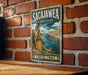 A vintage-style metal sign for Sacajawea State Park in Washington, featuring an illustration of a woman in traditional clothing and a scenic landscape.