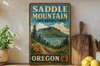 A vintage-style sign for Saddle Mountain State Natural Area in Oregon, featuring a scenic mountain landscape with a river and pine trees.
