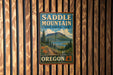 A vintage-style metal sign for Saddle Mountain, the State Natural Area in Oregon, is displayed on a wooden wall.