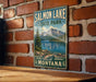 A vintage metal sign for Salmon Lake State Park in Montana, featuring a scenic landscape with mountains, a lake, and a pine tree.