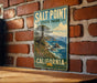 A vintage-style metal sign for Salt Point State Park in California, featuring a scenic coastal landscape with a tree and ocean in the background.