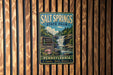 A vintage metal sign for Salt Springs State Park in Pennsylvania, featuring a waterfall and lush greenery, is displayed on a wooden wall.