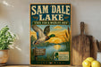 A vintage-style metal sign for Sam Dale Lake, featuring an illustration of a duck in flight over a lake and surrounding landscape, with text promoting the state's fish and wildlife area.