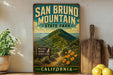 A vintage-style metal sign for San Bruno Mountain State Park in California, featuring a scenic mountain landscape with a trail leading to a wildlife viewing sign.