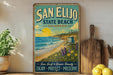 A vintage-style metal sign for San Elijo State Beach, California, featuring a beach scene with a lifeguard tower and a sunset over the ocean.