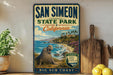 A vintage-style sign for San Simeon State Park in California, featuring a scenic image of a coastal landscape with a large seal.