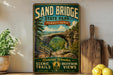 A vintage-style metal sign for Sand Bridge State Park in Pennsylvania, featuring a scenic image of the arch and the surrounding landscape.