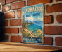 A vintage-style metal sign for Sand Harbor at Lake Tahoe, featuring a scenic landscape with mountains, water, and a clear blue sky.