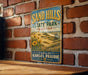 A vintage metal sign for Sand Hills State Park in Kansas, featuring a scenic landscape with a field of flowers and a mountain in the background.