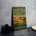 A vintage-style sign for Sand Hills State Park in Kansas, featuring a scenic landscape with a field of flowers and a blue sky.