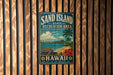 A vintage-style metal sign for the "Sand Island State Recreation Area" in Hawaii, featuring a beach scene with a palm tree, ocean, and city skyline.