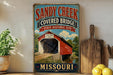 A vintage-style metal sign for the Sandy Creek Covered Bridge in Missouri, featuring an illustration of a covered bridge and the text "Sandy Creek Covered Bridge State Historic Site" and "Missouri".