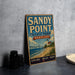 A vintage-style sign for Sandy Point State Park in Maryland, featuring a lighthouse and beach scene, is displayed on a gray countertop next to some black camera lenses.