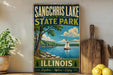A vintage-style sign for Sangchris Lake State Park in Illinois, featuring a scenic image of a lake with a sailboat and trees.