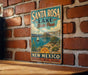 A vintage-style metal sign for Santa Rosa Lake State Park in New Mexico, featuring a scenic landscape with a sailboat and mountains in the background.