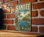 A vintage-style metal sign for Santee State Park in South Carolina, featuring a scenic illustration of a lake, palm trees, and a crane.