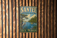 A vintage metal sign for Santee State Park, featuring a scenic illustration of a river, trees, and a bird, is displayed on a wooden wall.