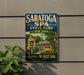 A vintage-style metal sign for Saratoga Spa, New York, with a scenic illustration of the spa and surrounding landscape.