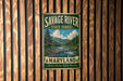 A vintage metal sign for Savage River State Forest in Maryland, featuring a scenic landscape with a river and pine trees.
