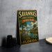 A vintage-style sign for Savannas Preserve State Park in Florida, featuring a bird and palm trees, is displayed on a gray concrete surface.