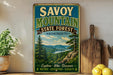 a vintage-style sign for Savoy Mountain State Forest in Massachusetts, with a scenic mountain landscape and a river in the background. The sign is displayed on a shelf next to a wooden cutting board and some potted plants.