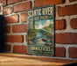 A vintage-style metal sign for Scantic River State Park in Connecticut, featuring a scenic illustration of a river surrounded by trees and mountains.