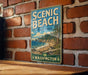 A vintage-style metal sign for Scenic Beach State Park in Washington, featuring a scenic illustration of the park's landscape.