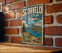 A vintage-style metal sign for Scofield State Park in Utah, featuring a scenic mountain landscape with a lake and a boat.
