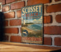 A vintage metal sign for "Scusset Beach State Reserve" in Massachusetts, featuring a lighthouse and beach scene.