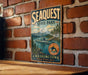 A vintage-style metal sign for Sequest State Park, featuring a scenic mountain landscape and a seascape with a boat.