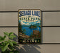 A vintage-style metal sign for Sebago Lake State Park in Maine, featuring a scenic landscape with a lake, mountains, and pine trees.