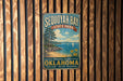 A vintage metal sign for Sequoyah Bay State Park, featuring a scenic landscape with a beach, mountains, and sailboats.