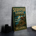 A vintage metal sign for the Sequoyah Lodge in Oklahoma, featuring a scenic illustration of the lodge and surrounding landscape.