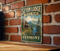A vintage-style metal sign for Seyon Lodge State Park in Vermont, featuring a scenic illustration of a cabin surrounded by nature.