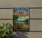 A vintage-style sign for Shabbona Lake, Illinois, featuring a scenic image of the lake and surrounding landscape.