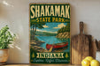 A vintage-style sign for Shakamak State Park in Indiana, featuring a red canoe on a lake surrounded by trees and mountains.