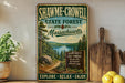 A vintage-style metal sign for Shawme-Crowell State Forest in Massachusetts, featuring a scenic illustration of pine trees, a lake, and a trail sign.