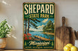 A vintage-style sign for Sheppard State Park in Mississippi, featuring a scenic image of a lake, dock, and surrounding nature.
